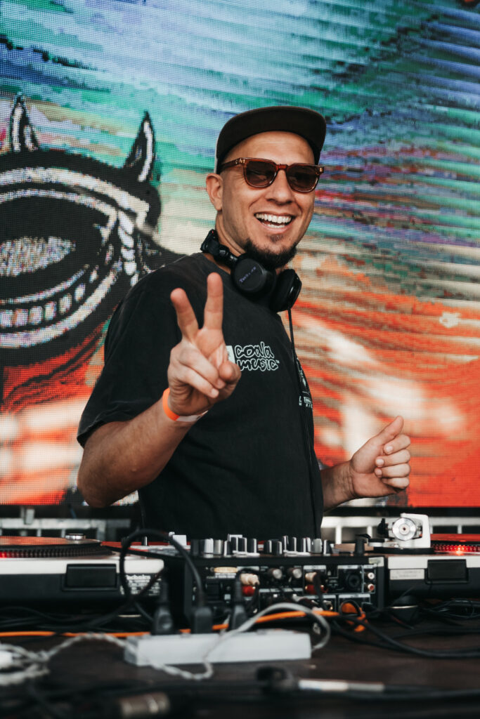 DJ Pezão sorrindo para as cameras e fazendo o sinal de "V", da paz, com as mãos.